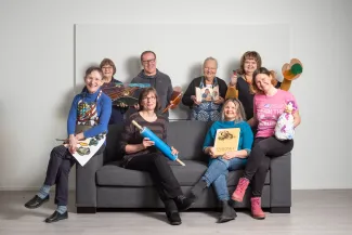 Soisalo-opiston kuvataiteet opettajia, osa istuu sohvalla ja osa sohvien kaiteilla sekä osa seisoo sohvan takana. Opettajilla käsissään kuvataiteen materiaaleja.