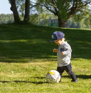 Pieni poika pelaamassa palloa kesäisenä päivänä puistossa.
