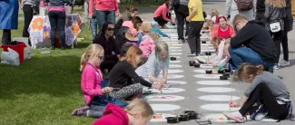 Ihmiset puistossa, lapset piirtää katuliiduilla asvalttiin.