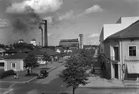 Valokuvaamo Jäniksen kuva Varkauden Ahströminkadulta, kesäkuva, katumaisema, keskellä kuvaa auto, taustalla tehdasmaisema