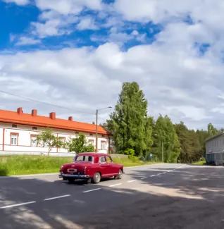 Punainen vanha auto kesäisenä päivänä tiellä.