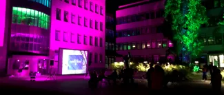 Kaupungintalo valaistuna violetinsävyillä. Puita ja ihmisiä.