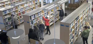 Asiakkaita kirjastossa kirjahyllyjen luona.