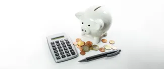 Valkoinen säästöpossu, laskin, kolikoita ja kynä.