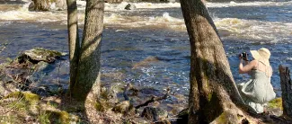 Tyttö valokuvaa Ämmäkosken rannalla luontoa.