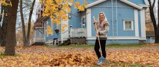 Nainen haravoi lehtiä puutalon pihalla.
